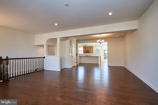 a view of an empty room with wooden floor and a kitchen