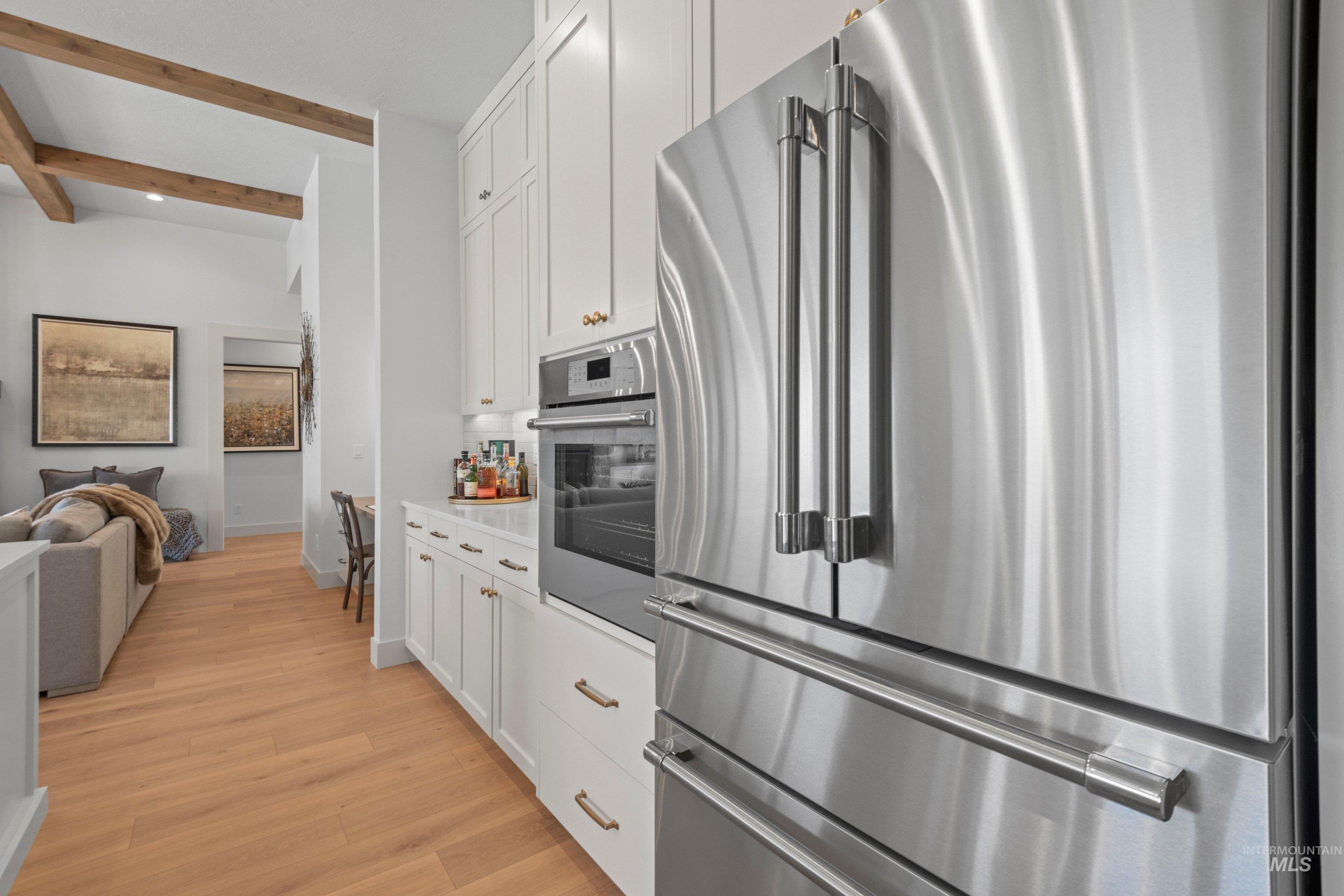 24990 Belgian Way Middleton, ID 83644 - Photo 14 of 50 Stainless steel refrigerator and built-in oven, white cabinetry with gold-tone hardware, light wood-finish flooring, and exposed ceiling beams