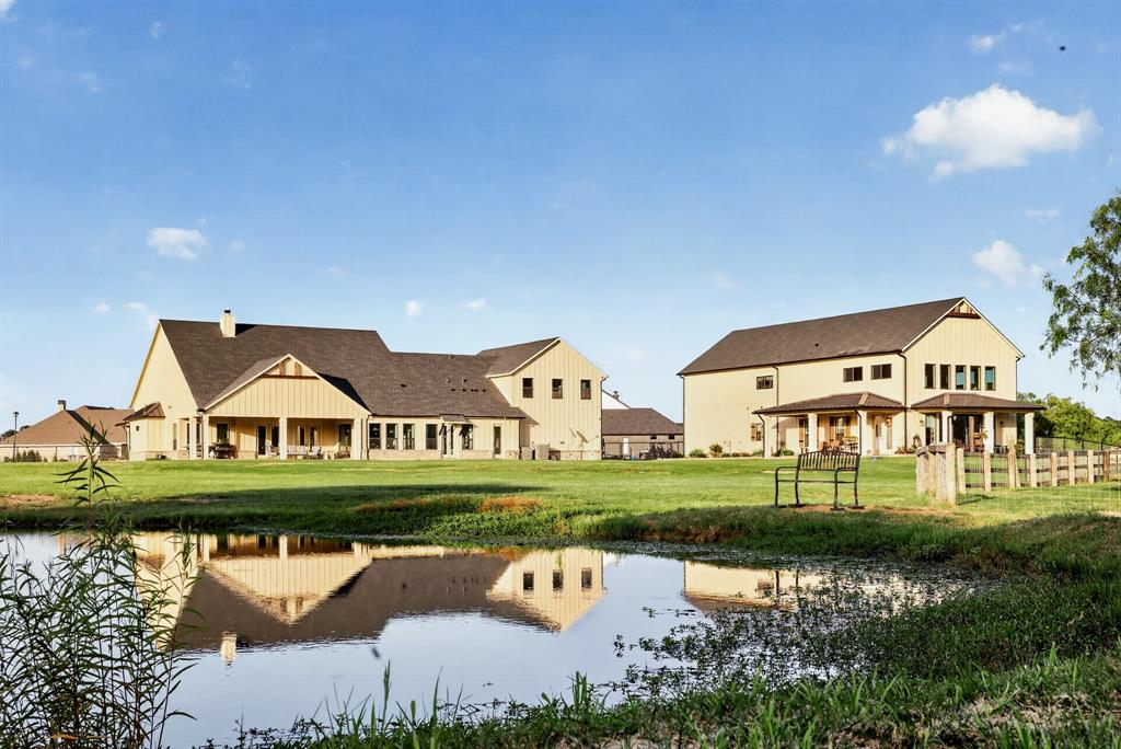 985 Vest Lane Pilot Point, TX 76258 - Photo 3 of 40 Expansive property featuring a tranquil pond with reflective waters, two distinct structures with pitched roofs, and a verdant lawn