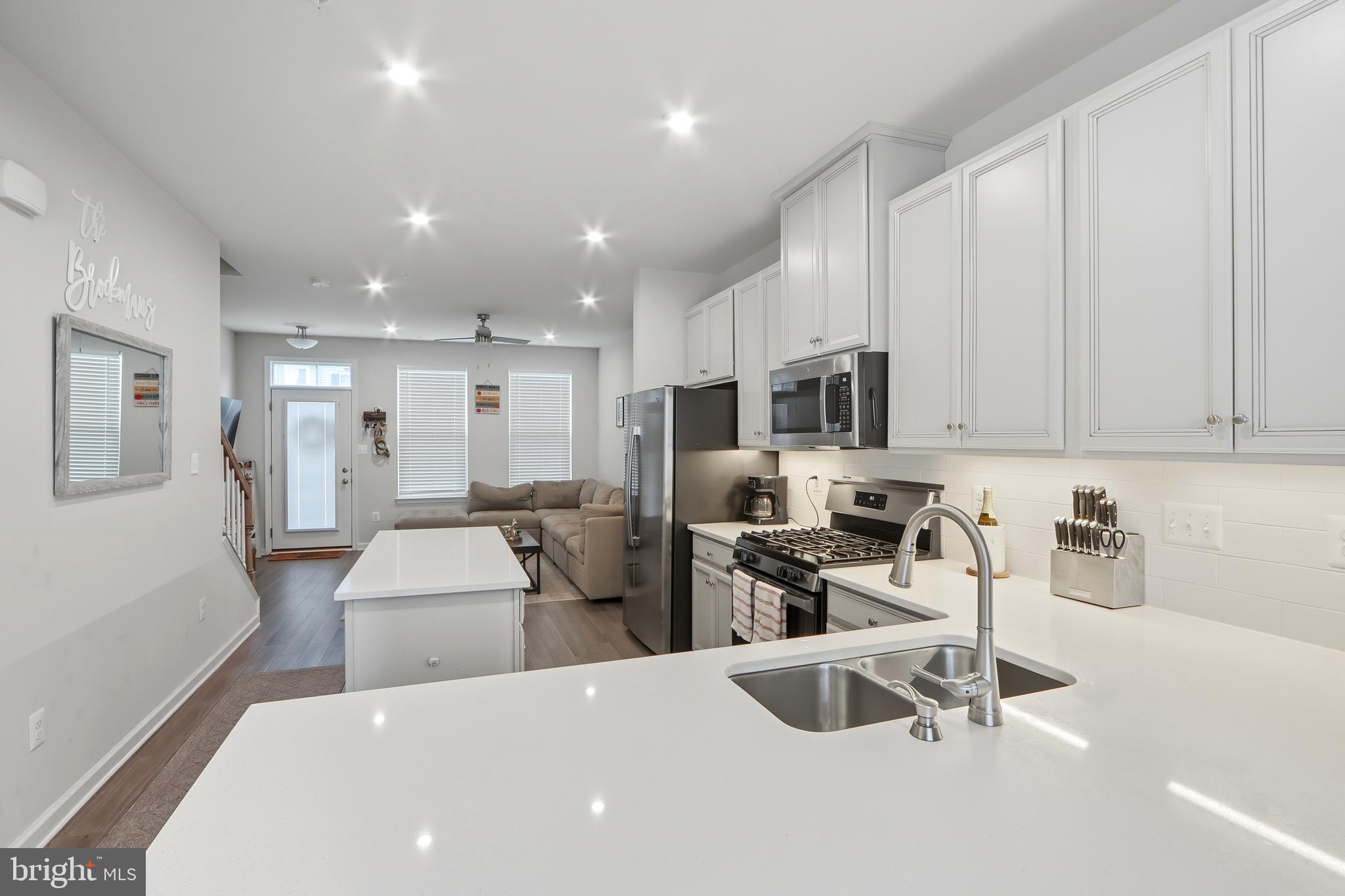 3458 Jacobs Ford Way Hanover, MD 21076 - Photo 9 of 39 a large white kitchen with stainless steel appliances a stove a sink a refrigerator white cabinets and couches with wooden floor