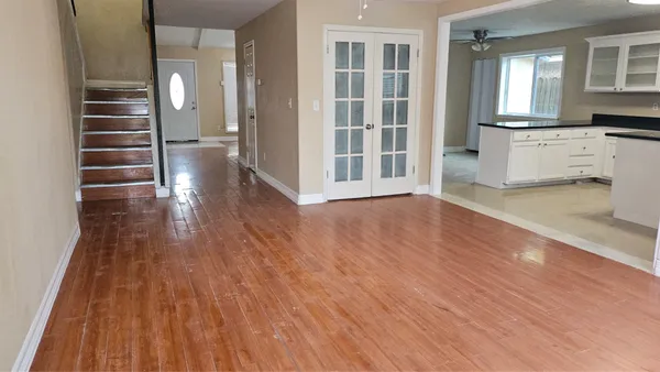 a view of empty room with wooden floor and kitchen