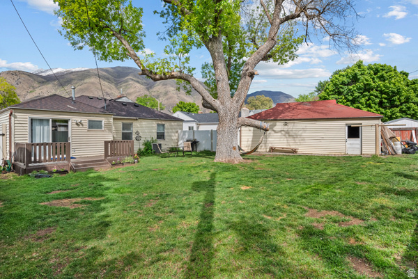 88 East C Street Springville, UT 84663 - Photo 28 of 32 Expansive backyard with a large mature tree, featuring a two-tier wood deck, light-colored siding on the main structure, and a detached outbuilding with a red roof