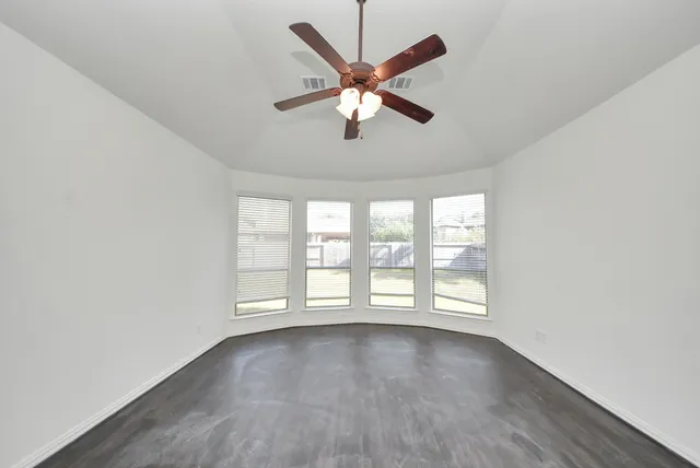 an empty room with wooden floor fan and windows