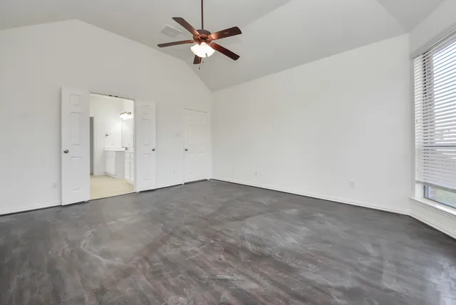 an empty room with chandelier fan and windows