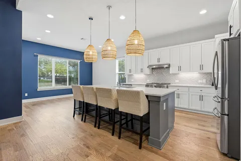 a kitchen with stainless steel appliances granite countertop a stove a refrigerator a kitchen island a sink dishwasher a dining table and chairs with wooden floor