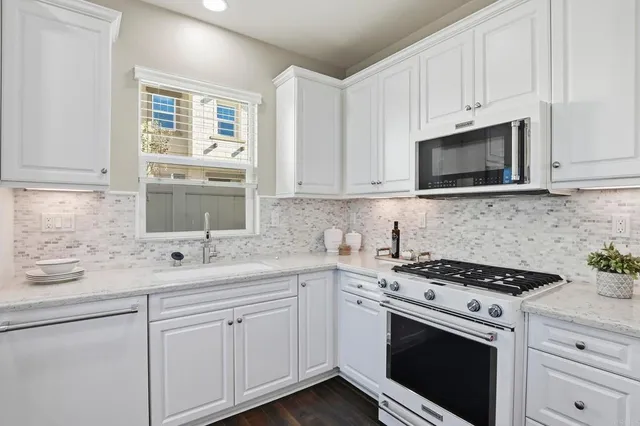 a kitchen with granite countertop white cabinets sink and appliances