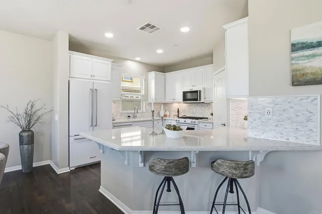 a kitchen with stainless steel appliances granite countertop a sink a stove a refrigerator a microwave oven with white cabinets and wooden floor