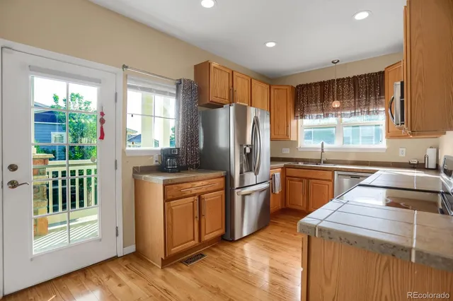 a kitchen with stainless steel appliances granite countertop a refrigerator a sink dishwasher a stove and a large window with wooden floor