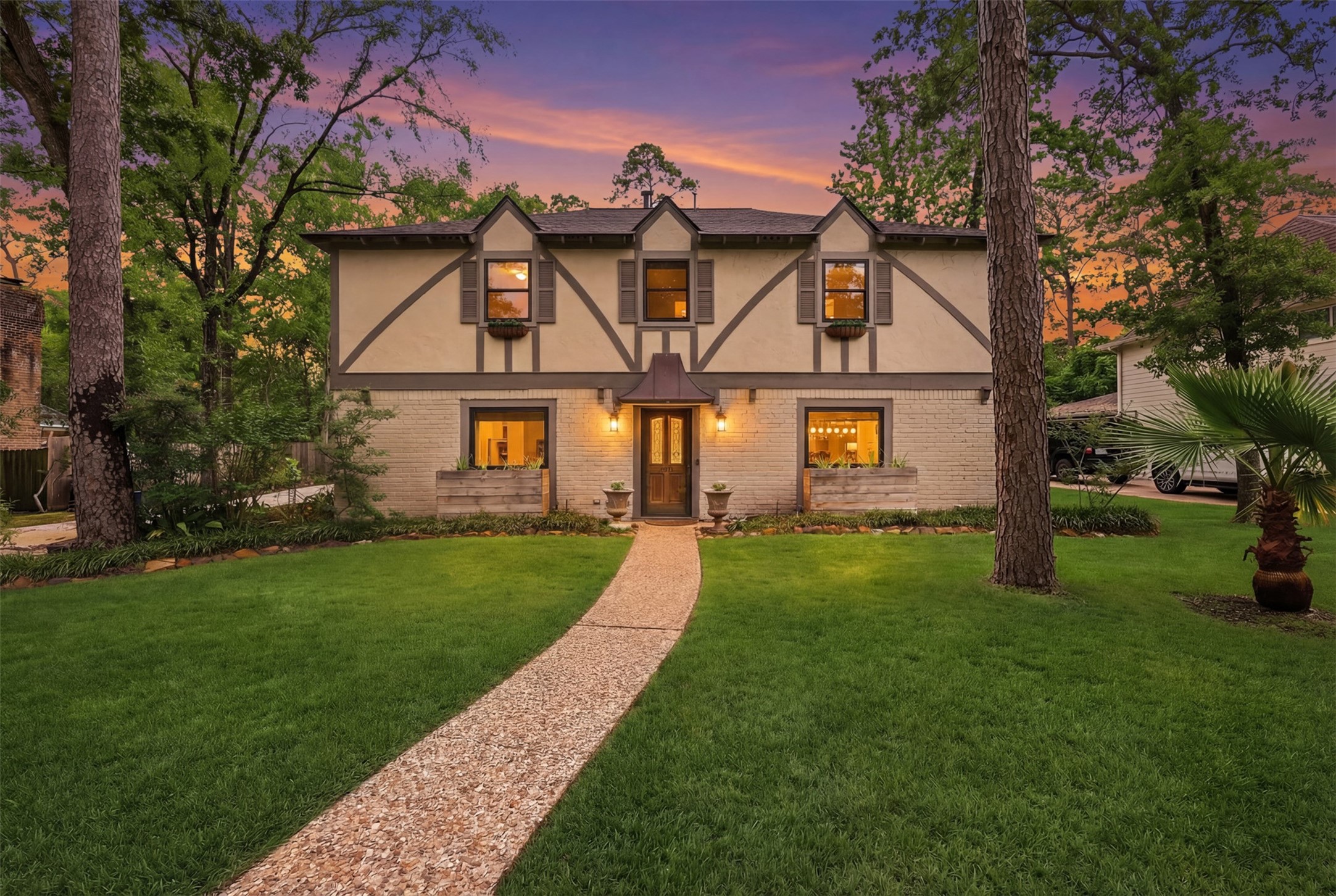 Charming view of the home at sunset with a welcoming entry and large mature trees.