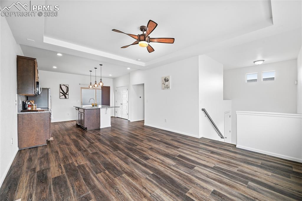 9414 Timberlake Loop Colorado Springs, CO 80927 - Photo 7 of 40 Unfurnished living room featuring a raised ceiling, a ceiling fan, and dark luxury vinyl wood-style floors