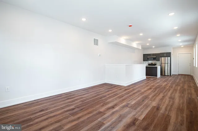 a view of empty room with wooden floor and kitchen