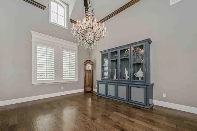 an empty room with wooden floor chandelier and windows