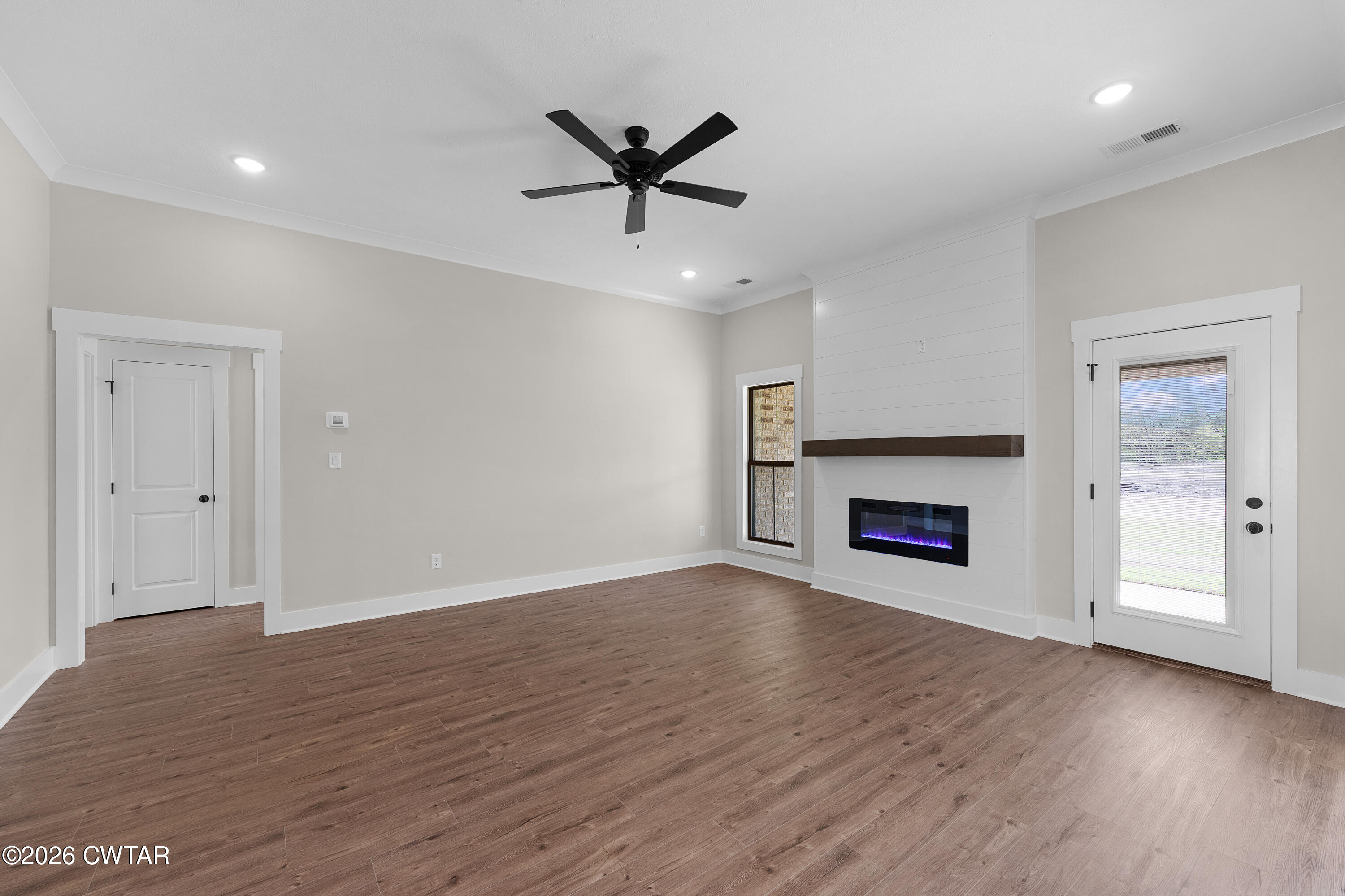 19 Emerald Downs Three Way, TN 38343 - Photo 3 of 17 an empty room with wooden floor a ceiling fan a fireplace and windows