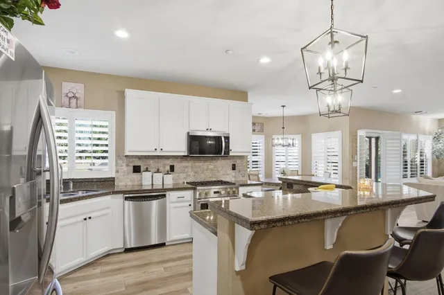 a kitchen with stainless steel appliances granite countertop a sink dishwasher a stove a refrigerator and island with wooden floor