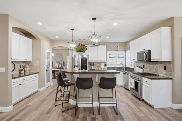 a kitchen with stainless steel appliances kitchen island granite countertop a stove a sink dishwasher a dining table and chairs with wooden floor