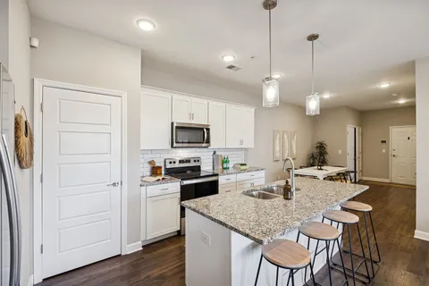 a kitchen with stainless steel appliances granite countertop a sink a stove a refrigerator a dining table with chairs and wooden floor