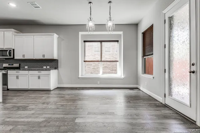 a kitchen with stainless steel appliances granite countertop a stove a sink and white cabinets with wooden floor next to windows