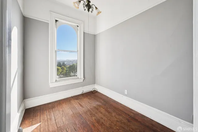an empty room with wooden floor staircase and windows