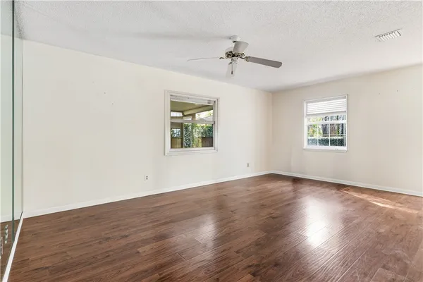 an empty room with wooden floor chandelier fan and windows