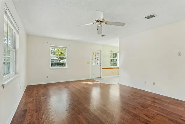 an empty room with wooden floor chandelier fan and windows