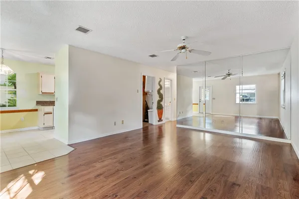 a view of an empty room with wooden floor and a kitchen