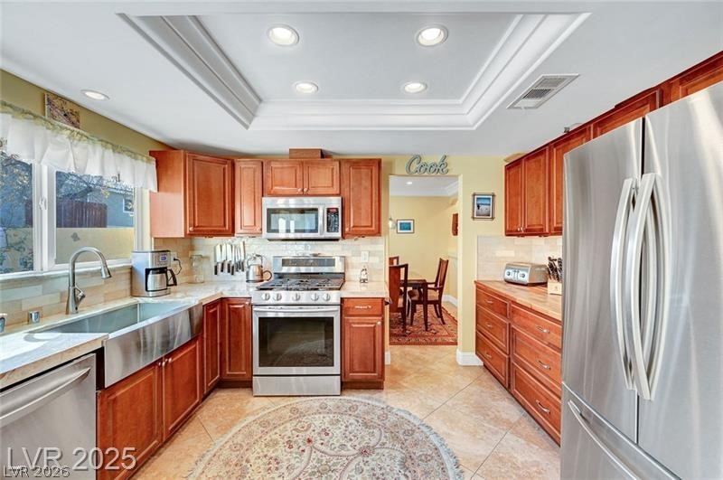 2410 Doherty Way Henderson, NV 89014 - Photo 21 of 63 Kitchen featuring stainless steel appliances, a tray ceiling, recessed lighting, light countertops, and tasteful backsplash