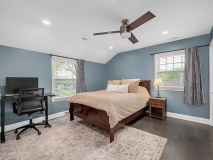 a bedroom with a bed a desk and chair with windows
