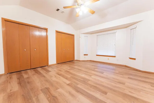 a view of an empty room with wooden floor and a ceiling fan