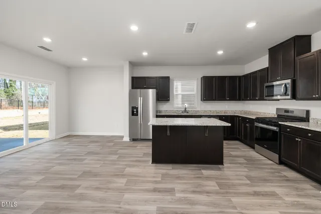 a large kitchen with stainless steel appliances granite countertop a stove a sink dishwasher a microwave oven and a refrigerator with wooden floor