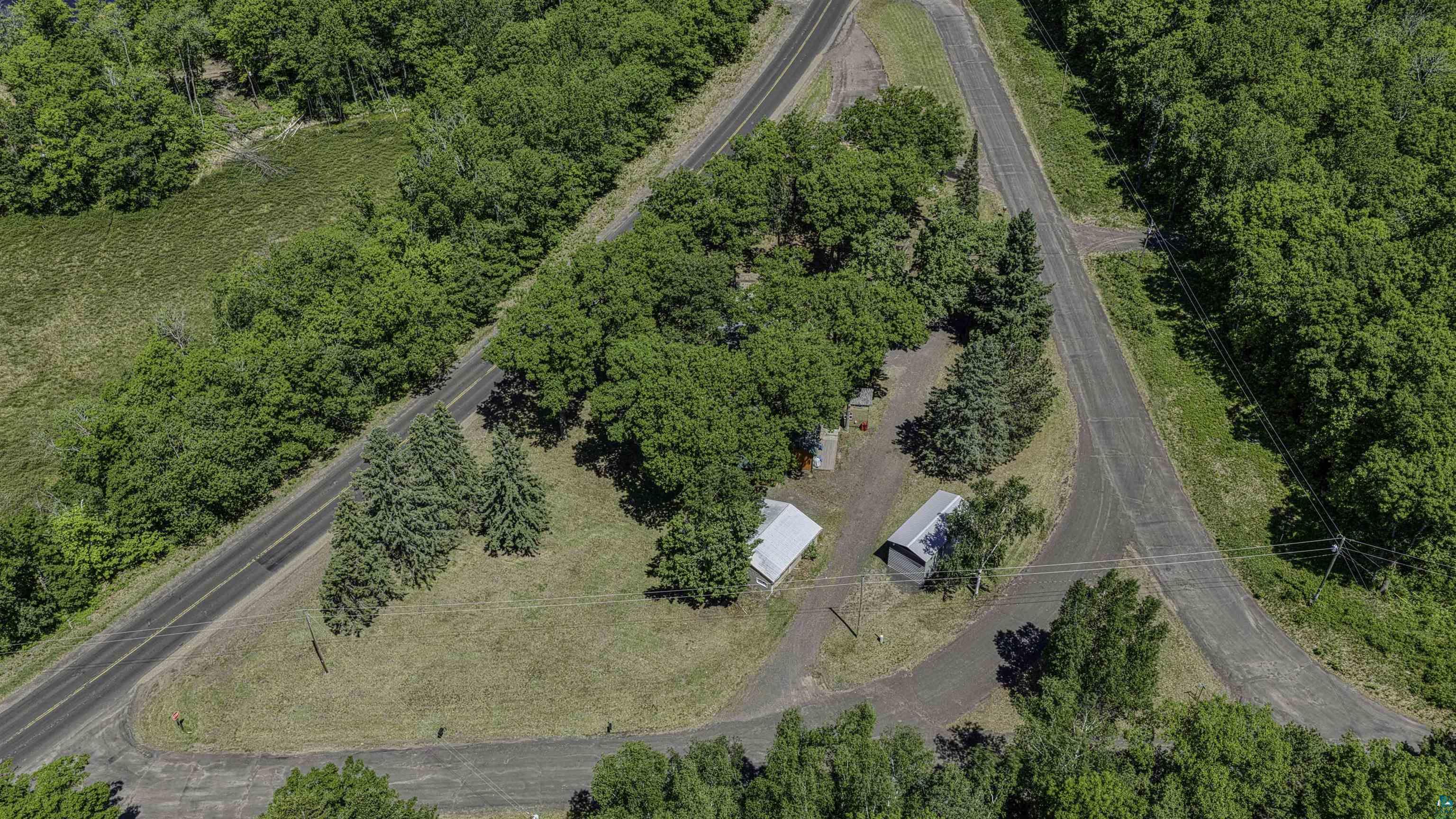 66075 Rooster Road Iron River, WI 54847 - Photo 10 of 52 Aerial perspective showcasing a property surrounded by mature trees, featuring two asphalt roads, two small outbuildings, and an expansive grassy area