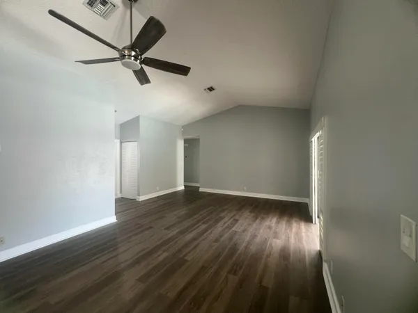 an empty room with wooden floor fan and windows