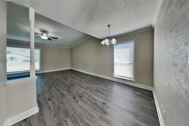 an empty room with wooden floor chandelier fan and windows