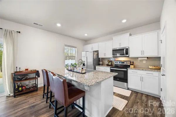 a kitchen with stainless steel appliances granite countertop a stove top oven a sink dishwasher and a dining table with wooden floor