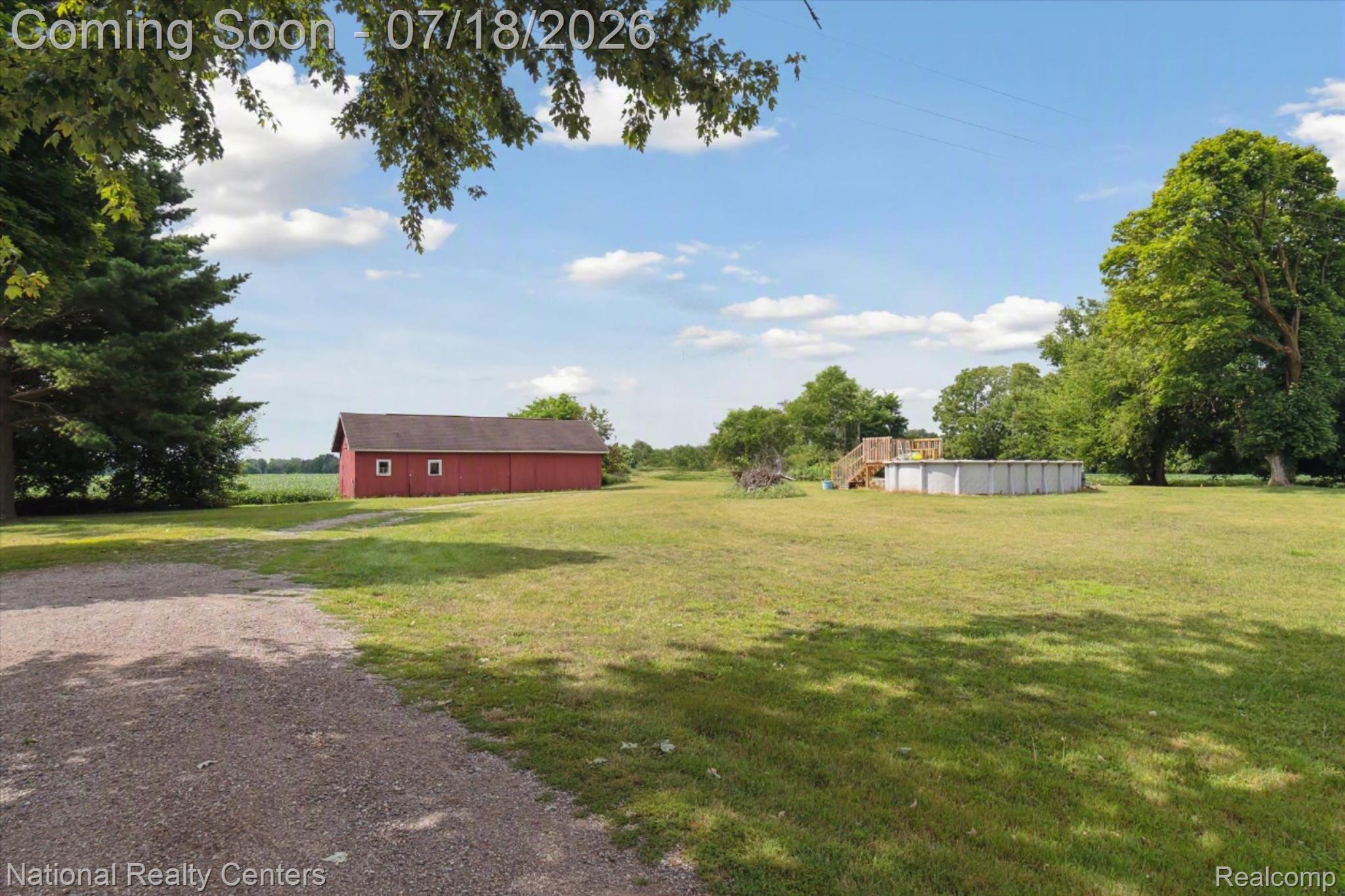 9589 Clinton Macon Road Tecumseh, MI 49286 - Photo 39 of 48 Spacious property featuring a red barn, an above-ground pool with a wooden deck, mature trees, and a gravel driveway