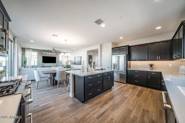 a kitchen with stainless steel appliances kitchen island granite countertop a refrigerator a stove top oven a sink dishwasher and a dining table with wooden floor