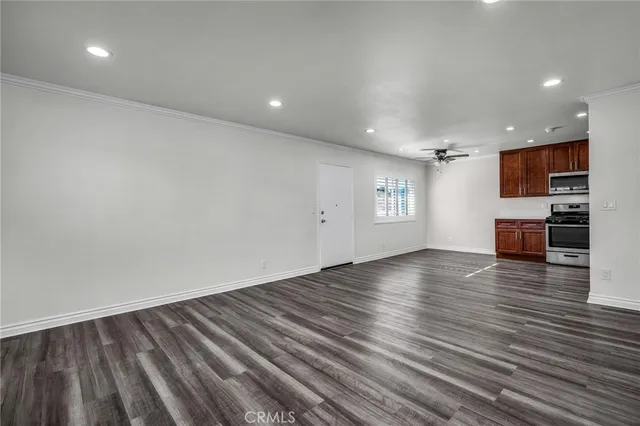 a view of empty room with wooden floor and kitchen