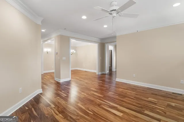 a view of an empty room with wooden floor and a ceiling fan