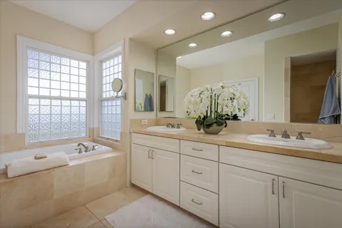 a spacious bathroom with double vanity a mirror a bathtub and window