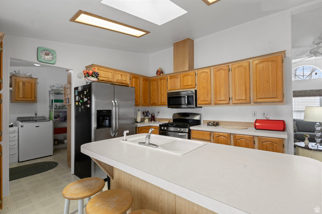 2600 North Hill Field Road, Unit 134 Layton, UT 84041 - Photo 12 of 41 Kitchen featuring light countertops, light floors, washer / clothes dryer, stainless steel appliances, and a kitchen breakfast bar