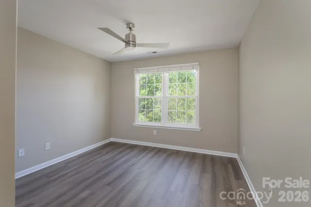 an empty room with wooden floor chandelier fan and windows