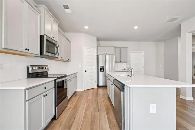 a kitchen with stainless steel appliances a stove top oven a sink a refrigerator white cabinets and wooden floor