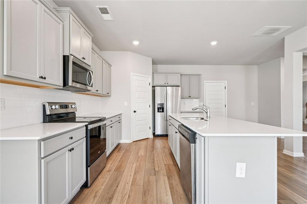 1547 Stinson Lane Locust Grove, GA 30248 - Photo 12 of 43 a kitchen with stainless steel appliances a stove top oven a sink a refrigerator white cabinets and wooden floor