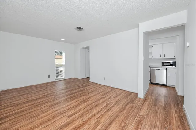 a view of empty room with wooden floor and kitchen