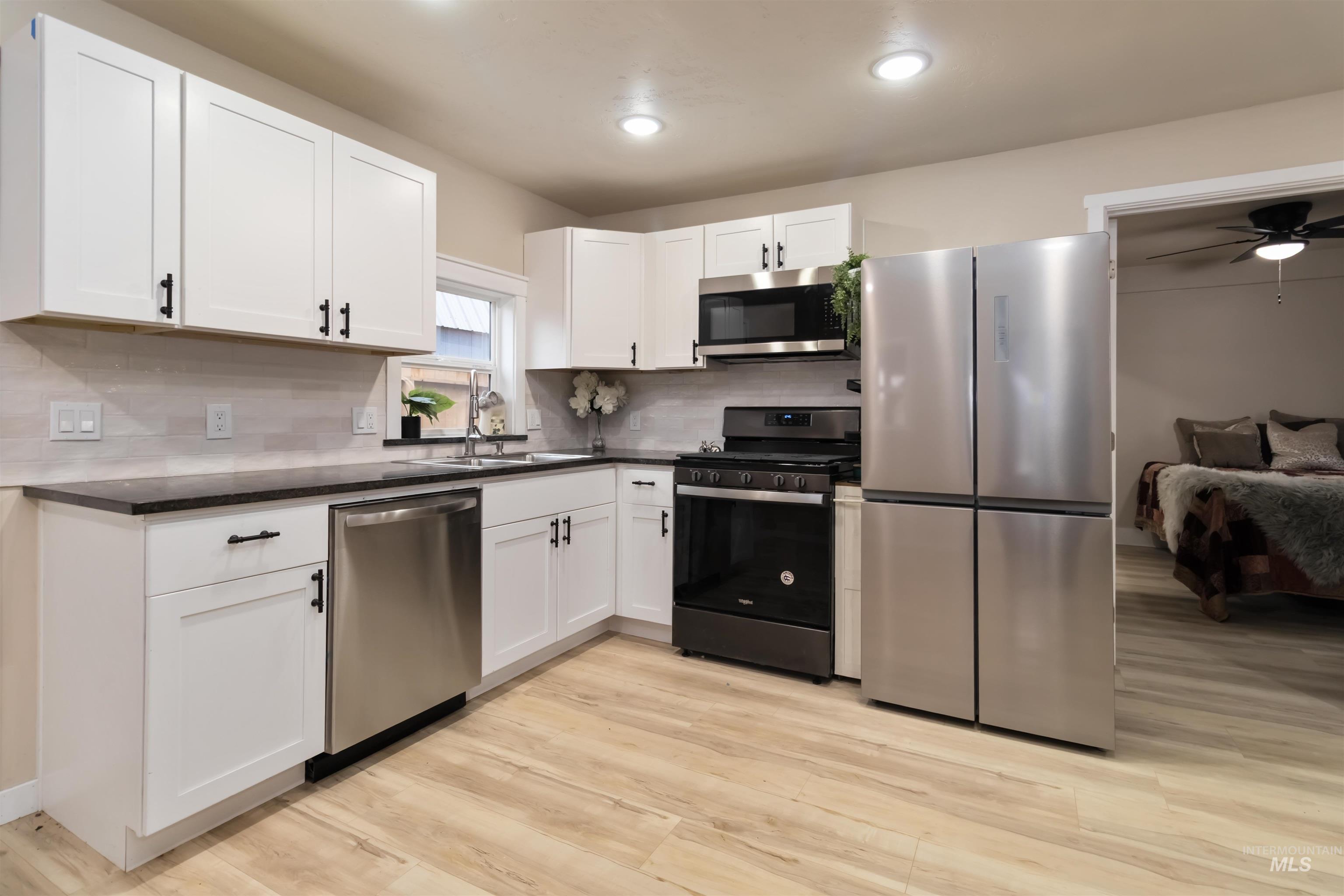 1012 East Main Street Weiser, ID 83672 - Photo 2 of 15 Kitchen featuring stainless steel appliances, white cabinetry, ceiling fan, and light wood-style flooring