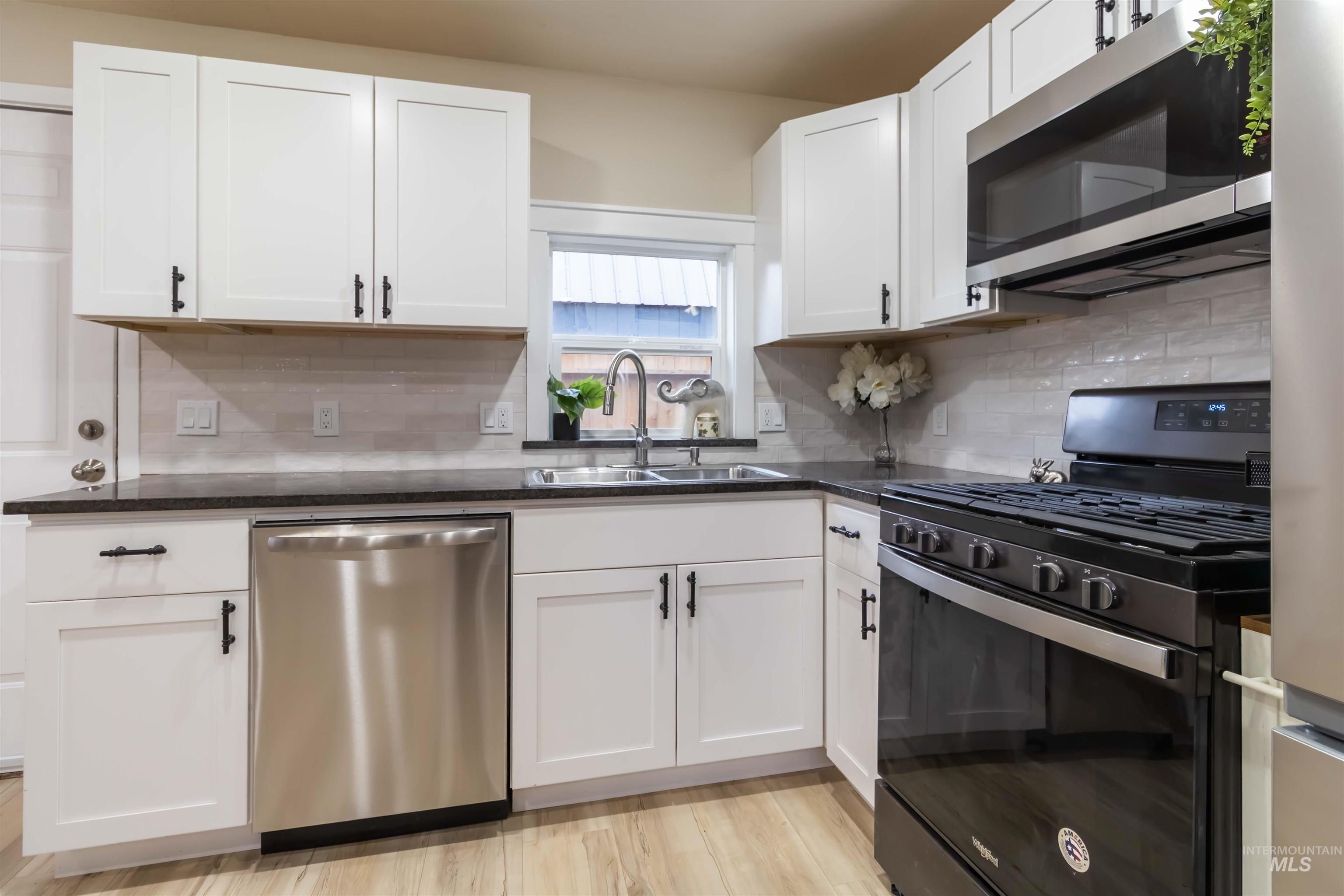 1012 East Main Street Weiser, ID 83672 - Photo 3 of 15 Kitchen featuring stainless steel appliances, white cabinets, dark stone counters, light wood-style flooring, and backsplash