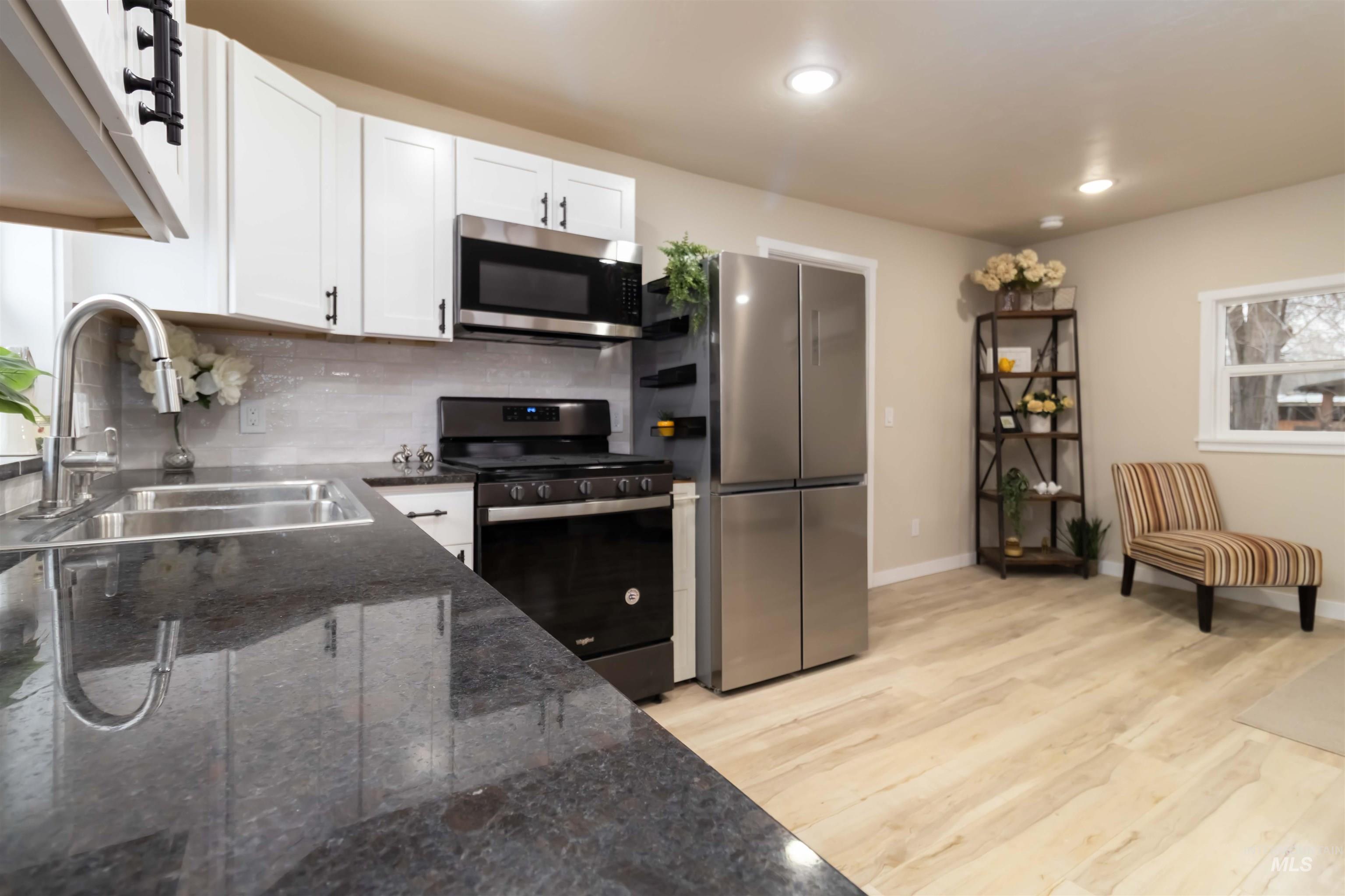 1012 East Main Street Weiser, ID 83672 - Photo 4 of 15 Kitchen with stainless steel appliances, light wood-type flooring, white cabinets, tasteful backsplash, and dark stone countertops