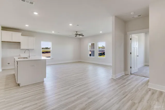 a view of an empty room and kitchen with wooden floor