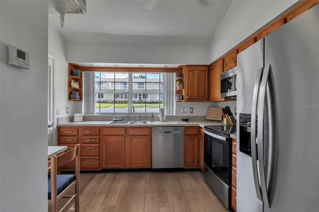 a kitchen with stainless steel appliances granite countertop a refrigerator a sink dishwasher a stove and white countertops with wooden floor