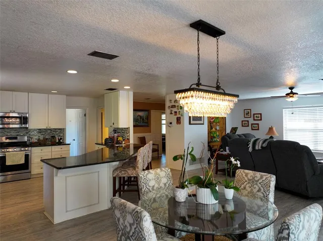 a kitchen with stainless steel appliances granite countertop a dining table chairs refrigerator and sink