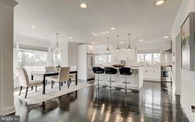 a kitchen with stainless steel appliances kitchen island granite countertop a stove a sink a refrigerator a dining table and chairs with wooden floor